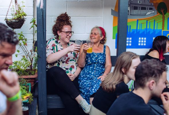 Two women smiling and enjoying their drinks in a busy beer-garden