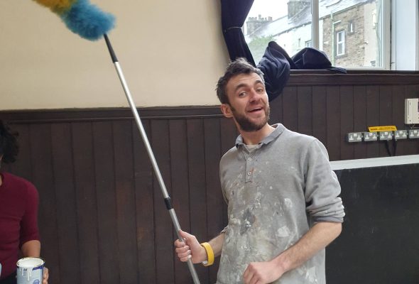 A man smiles excitedly whilst holding a long feather duster