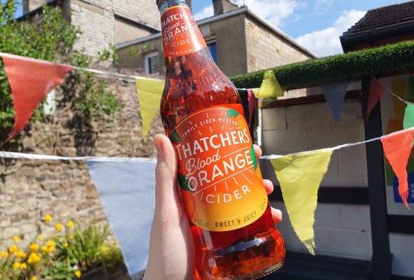 A bottle of Thatcher's Blood Orange being Held up in a sunny garden