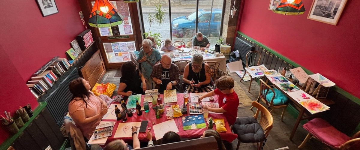 A group of people sat around a table full of art supplies in the Gregson Centre's Cafe Bar