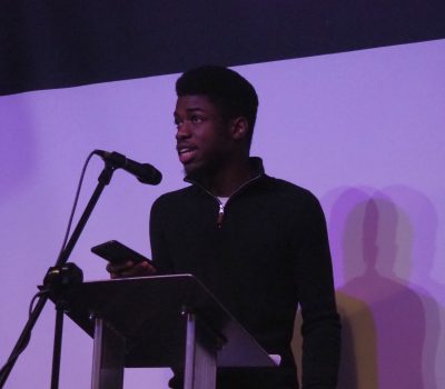 A young man stands at a podium with a microphone and reads
